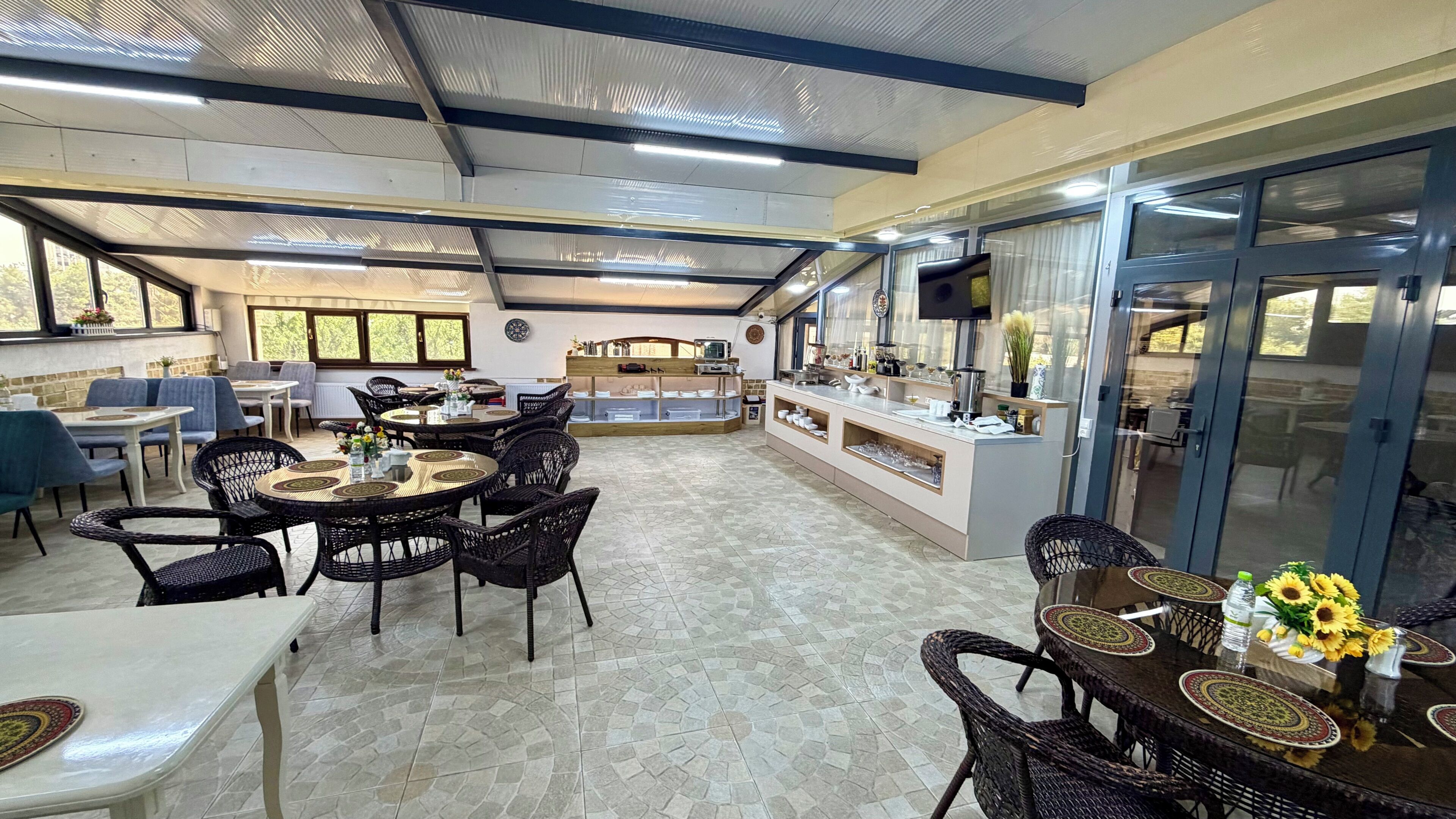 A spacious indoor dining area with round tables and chairs, a buffet counter, and large windows allowing natural light.