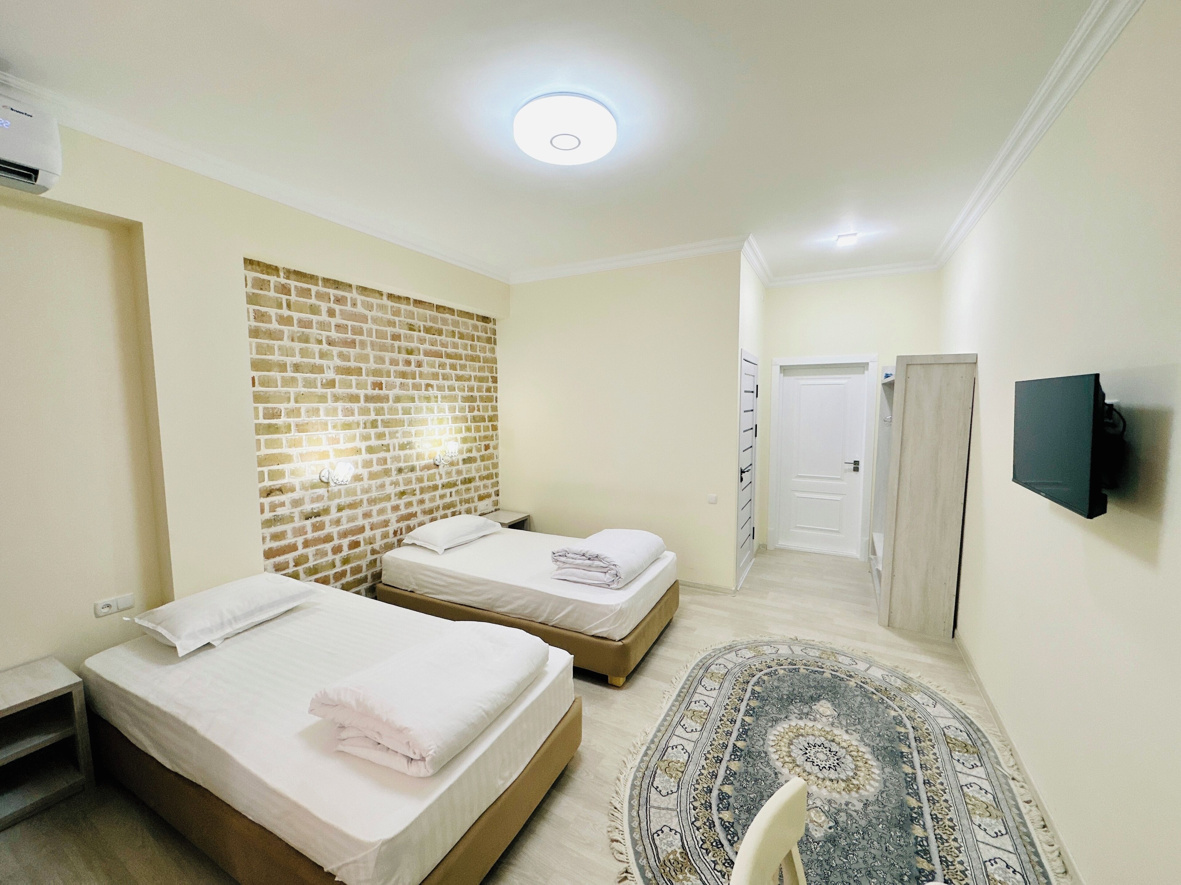 A hotel room with two beds, a brick accent wall, a flat-screen TV, and a patterned rug.