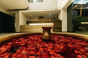 A reception area with a wooden reception desk, a vase with a decorative item, and a large bowl filled with red rose petals. - The Royale Senate Hebbal (Bengaluru)