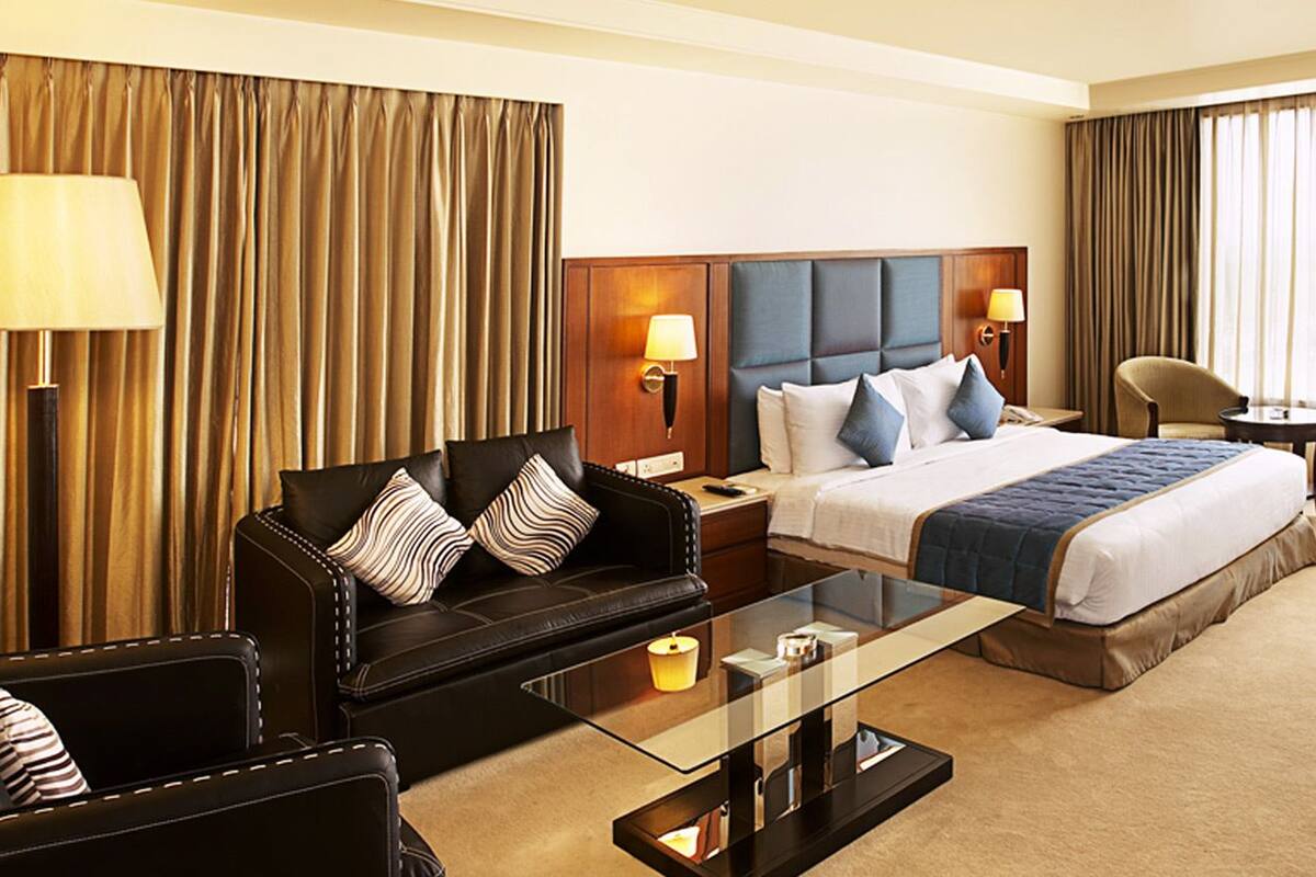 A hotel room with a bed, a sofa, a coffee table, a desk, and a chair.