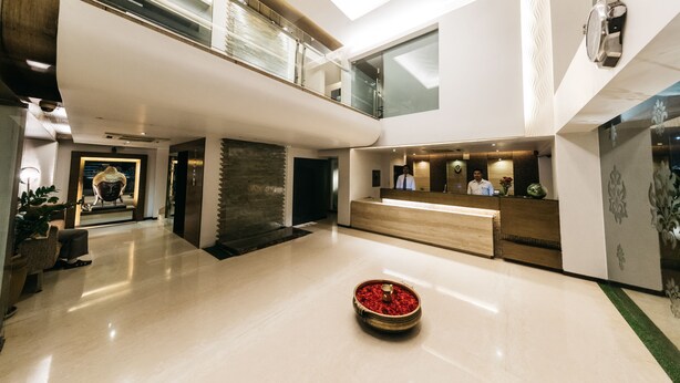 A spacious lobby with a reception desk, a seating area, and a decorative bowl with red flowers. - The Royale Senate Hebbal (Bengaluru)