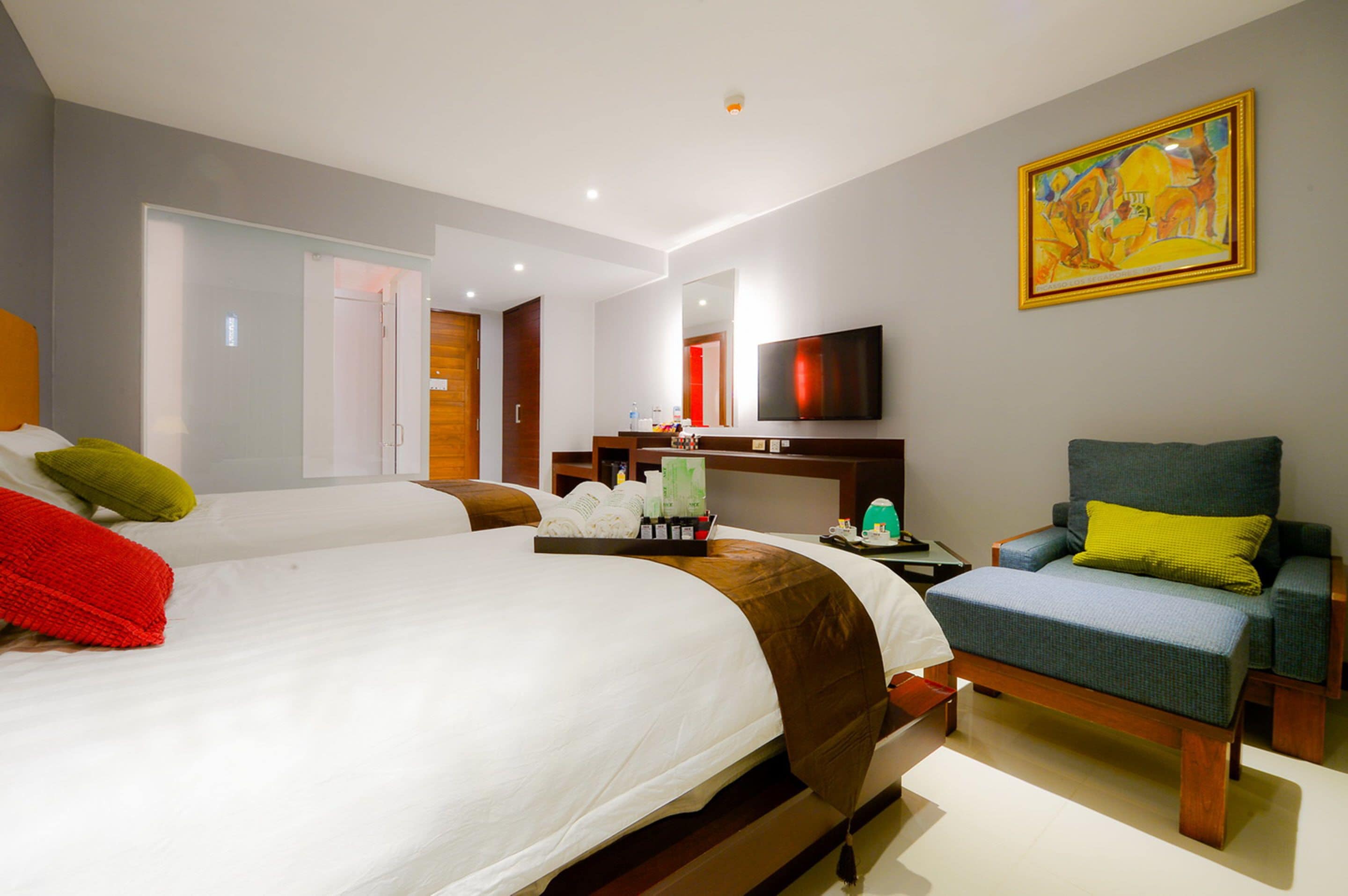 A hotel room with two beds, a TV, a painting, and a chair.