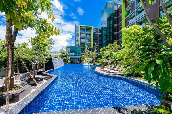 Una piscina con borde de azulejos, rodeada de árboles y edificios modernos.