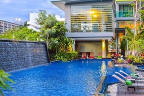 Un hotel moderno con piscina, zona de estar al aire libre y exuberante vegetación.