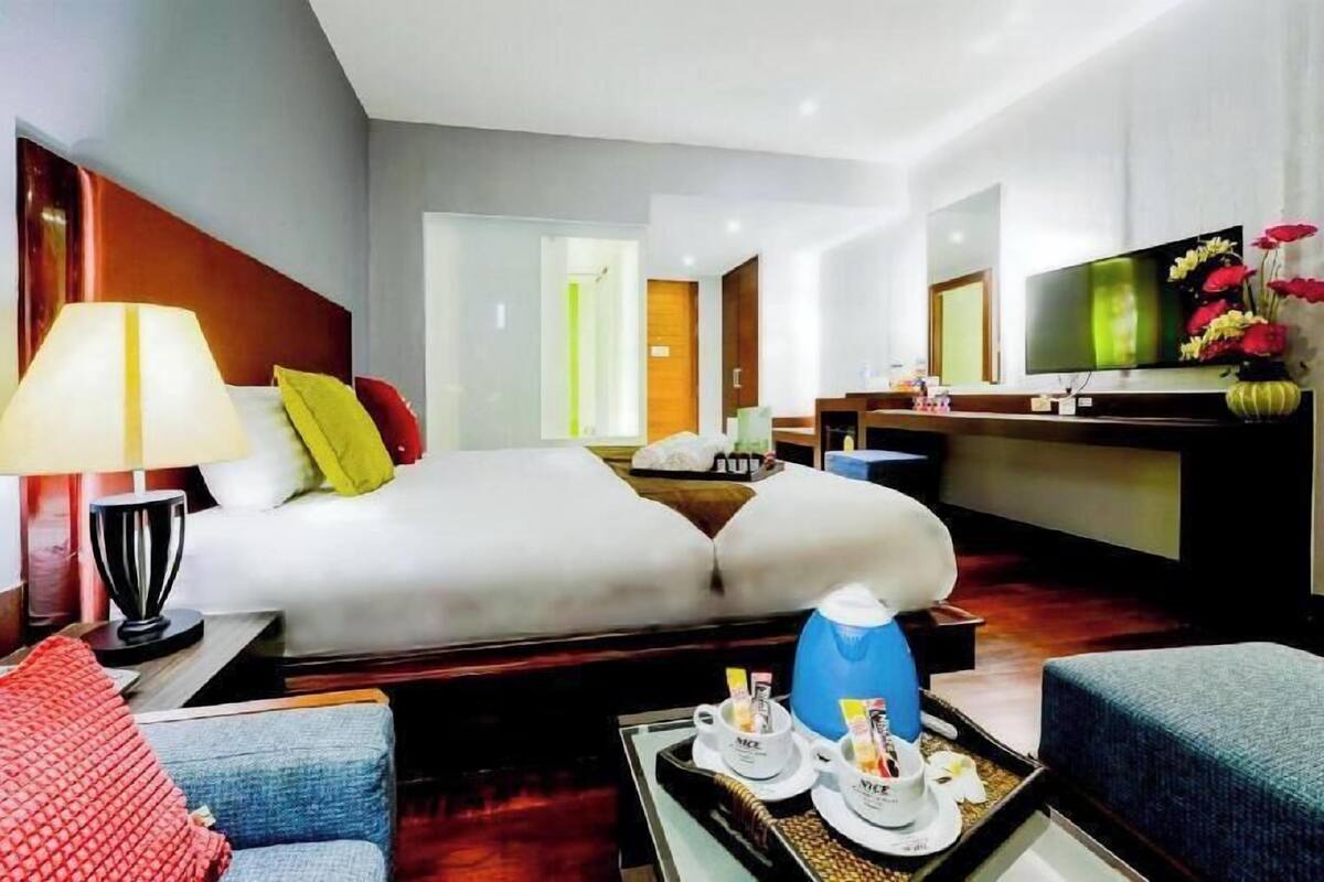 Una habitación de hotel con cama, mesita de noche, lámpara, televisor y escritorio con silla.