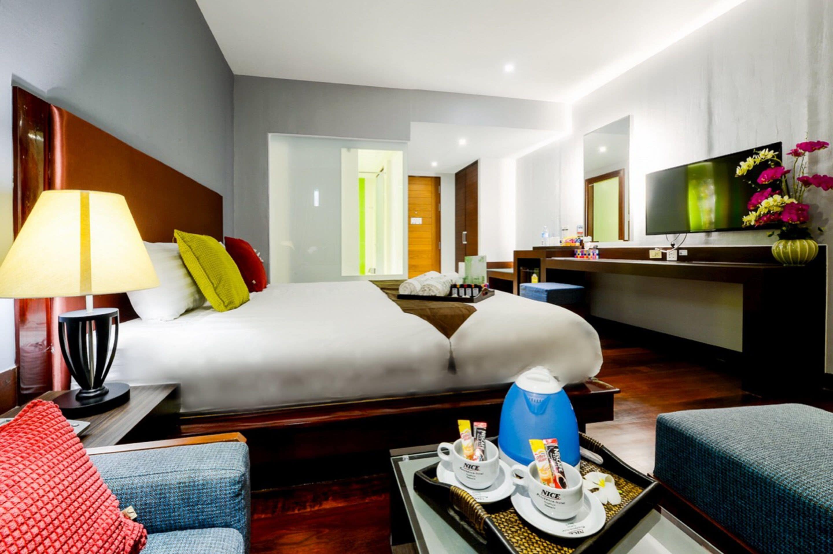 A hotel room with a bed, a desk with a computer, a TV, and a bathroom visible through an open door.