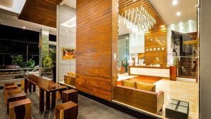 A modern hotel lobby with a wooden reception desk, seating area, and a large window offering a view of the outdoors. - Nice Residence Hotel Huahin (Hua Hin)