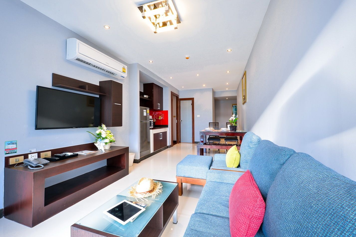 A modern living room with a flat-screen TV, a sofa, a coffee table, and a dining area in the background.