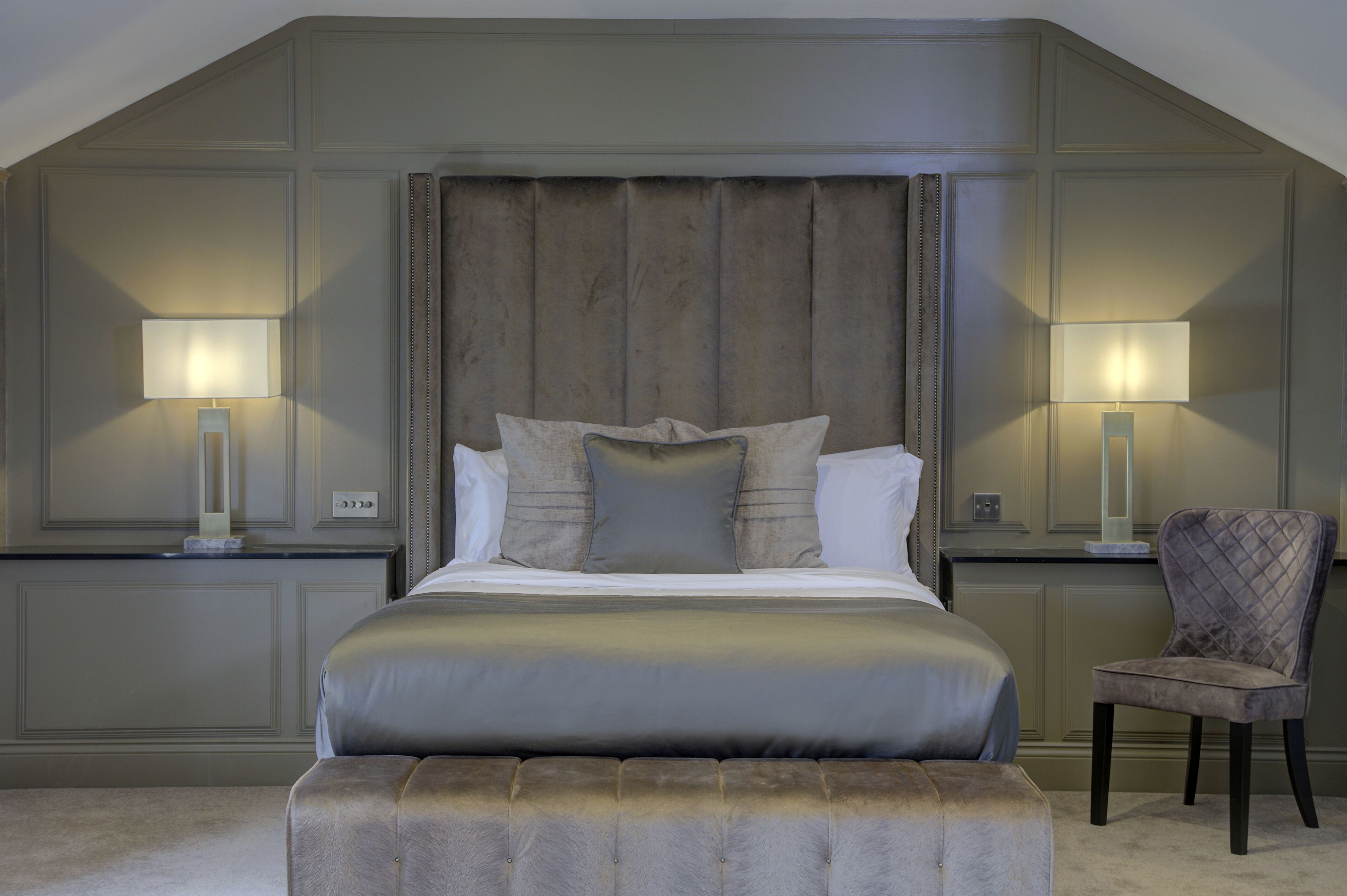 A bedroom with a large bed, two bedside tables, a chair, and a headboard.