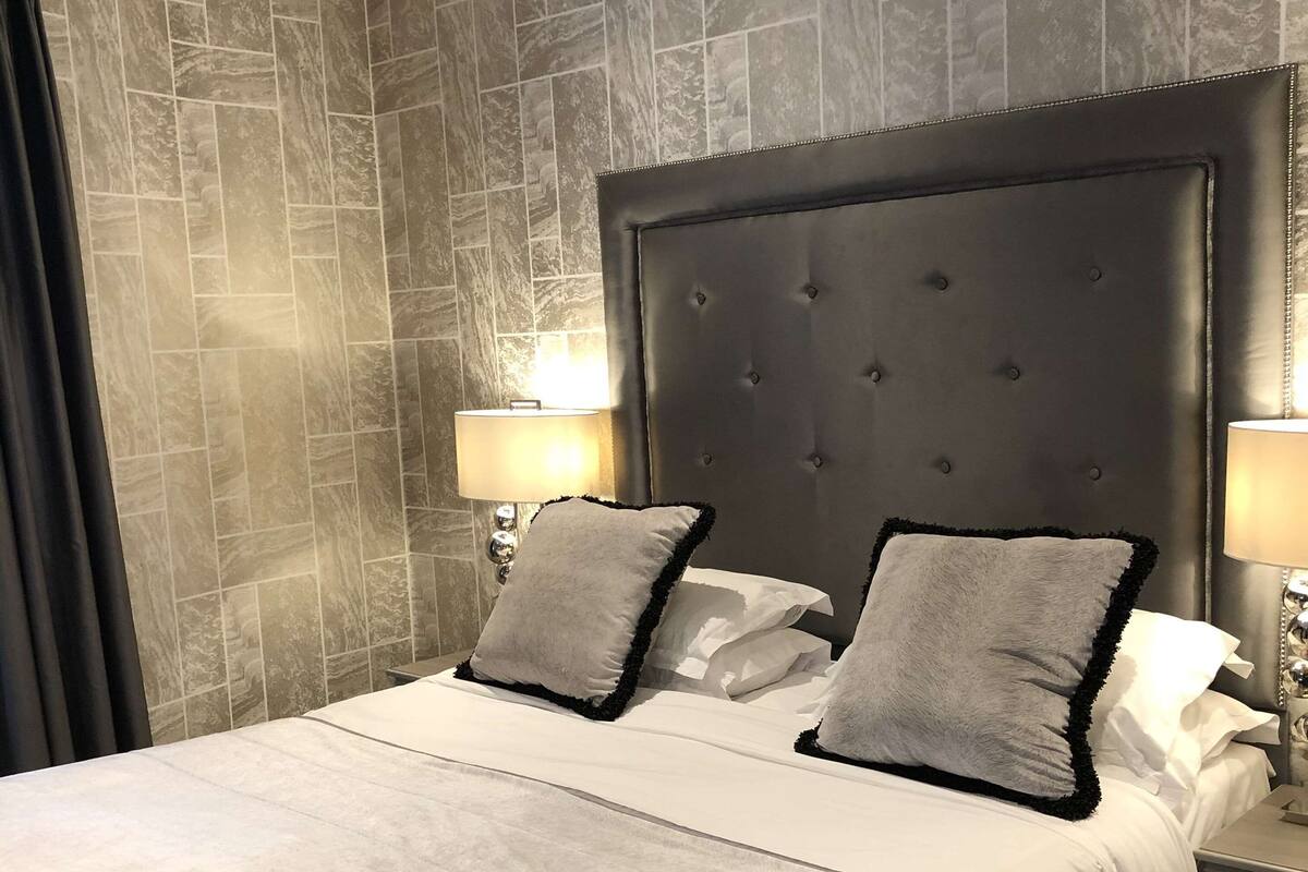 A modern hotel room with a large bed, two bedside lamps, and a dark headboard.