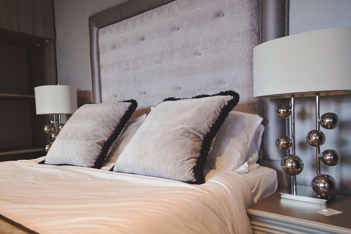 A neatly made bed with fluffy pillows, a tufted headboard, and two bedside lamps with spherical decorations.