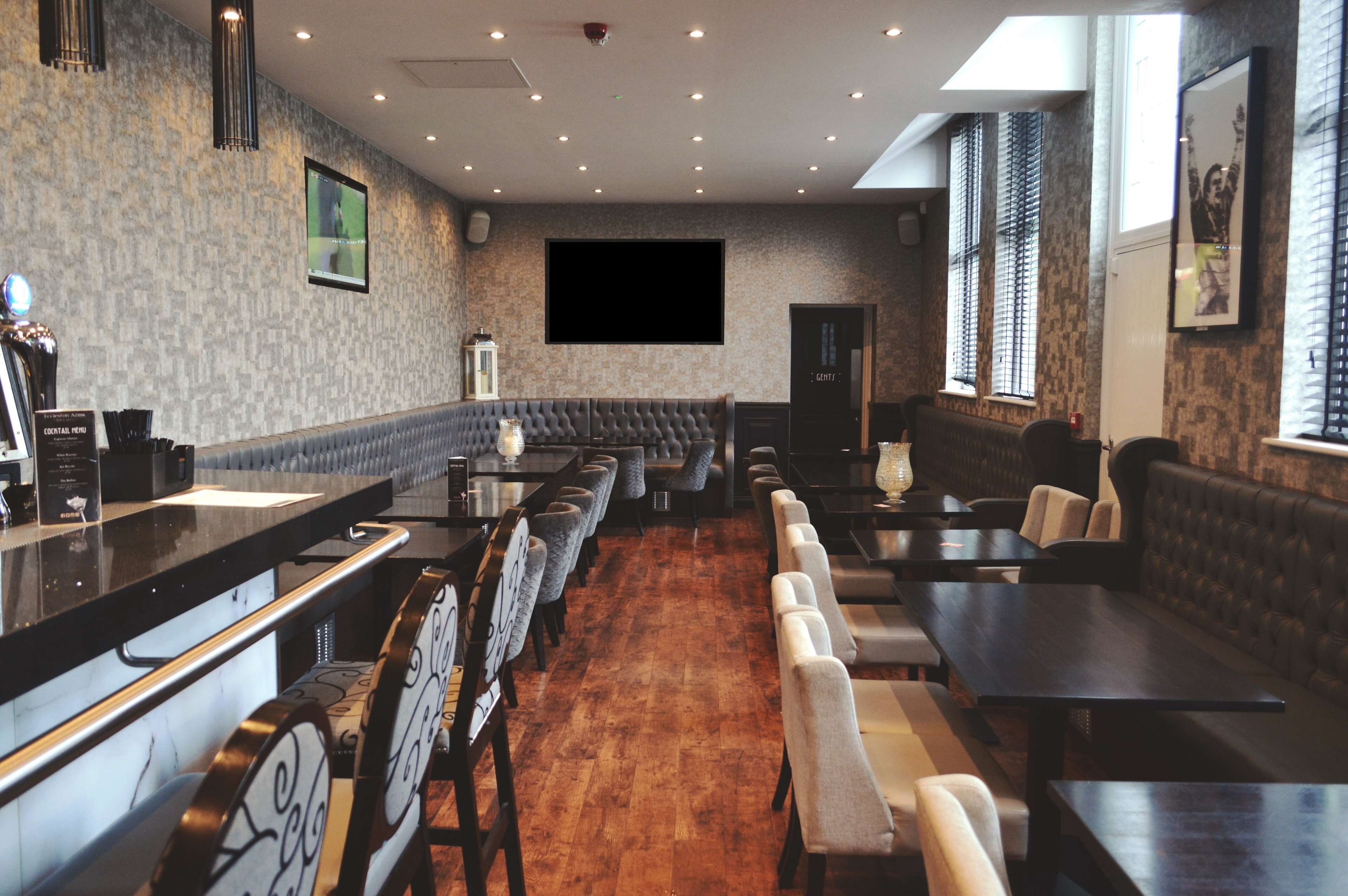 Un restaurante con una barra larga, varias zonas de estar y una gran pantalla de televisión en la pared.
