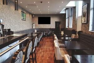 Un restaurante con una barra larga, varias zonas de estar y una gran pantalla de televisión en la pared.