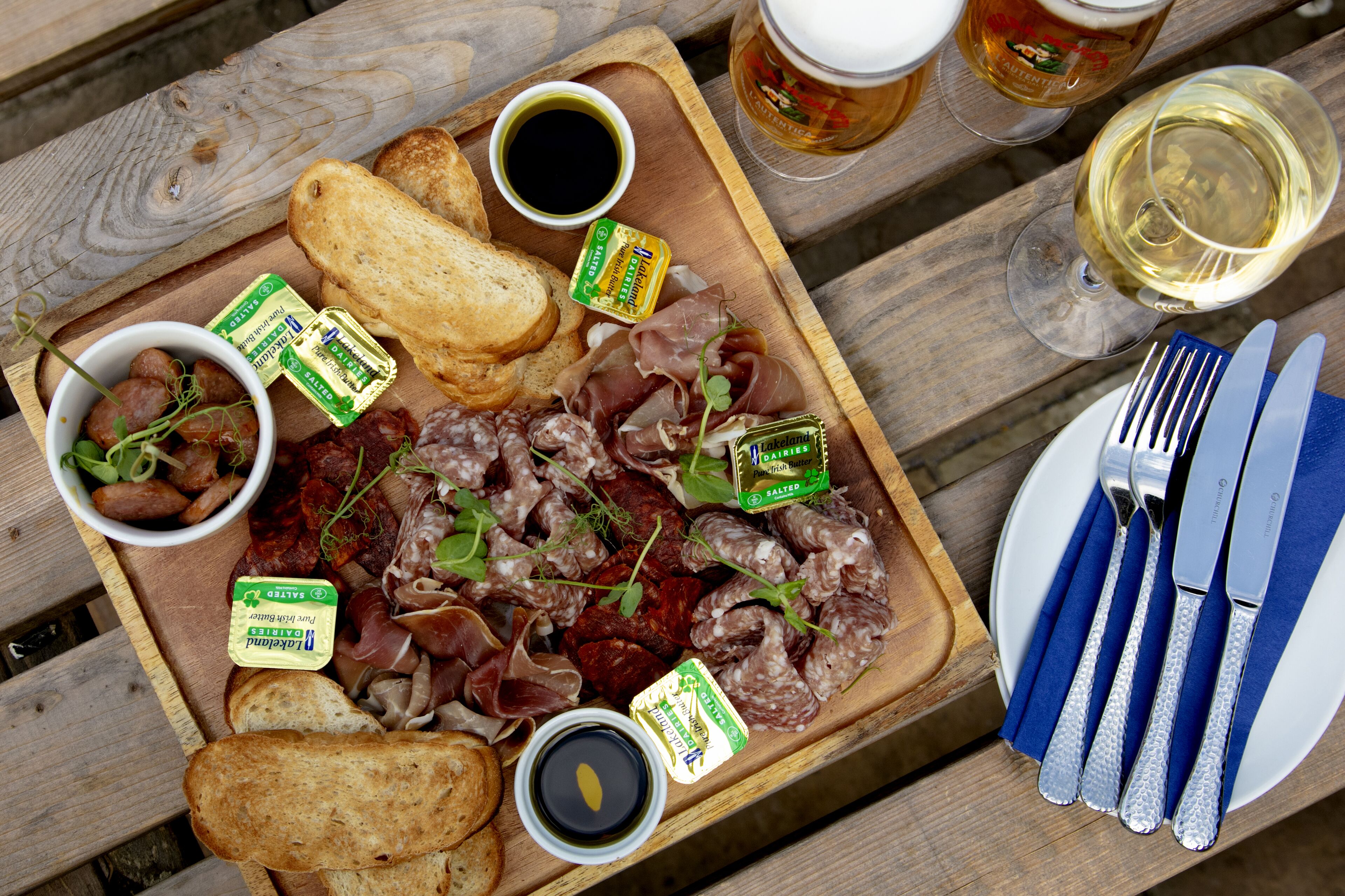 A wooden board with various meats, bread, and condiments.