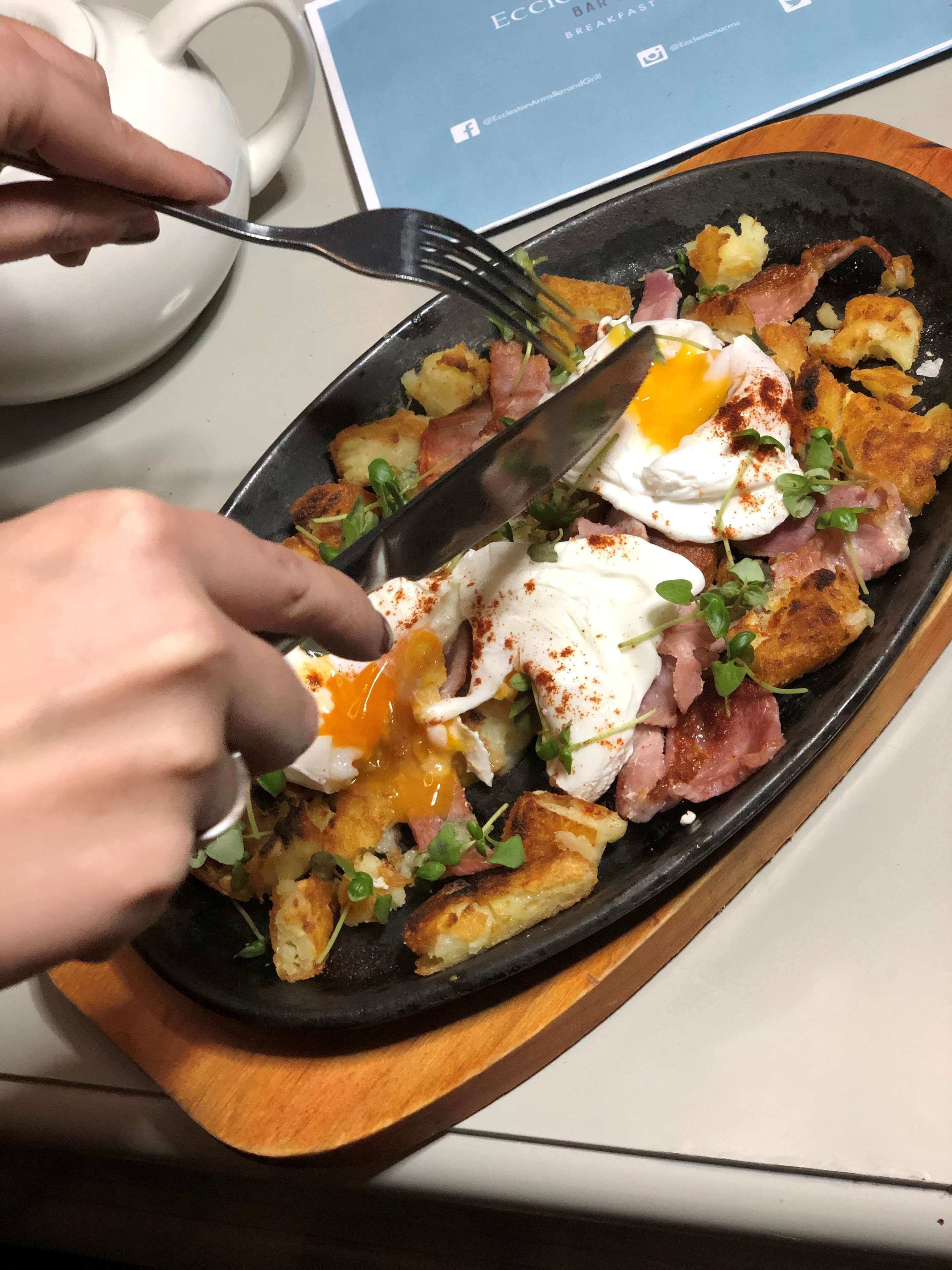 A breakfast dish with eggs, bacon, and potatoes on a black plate.