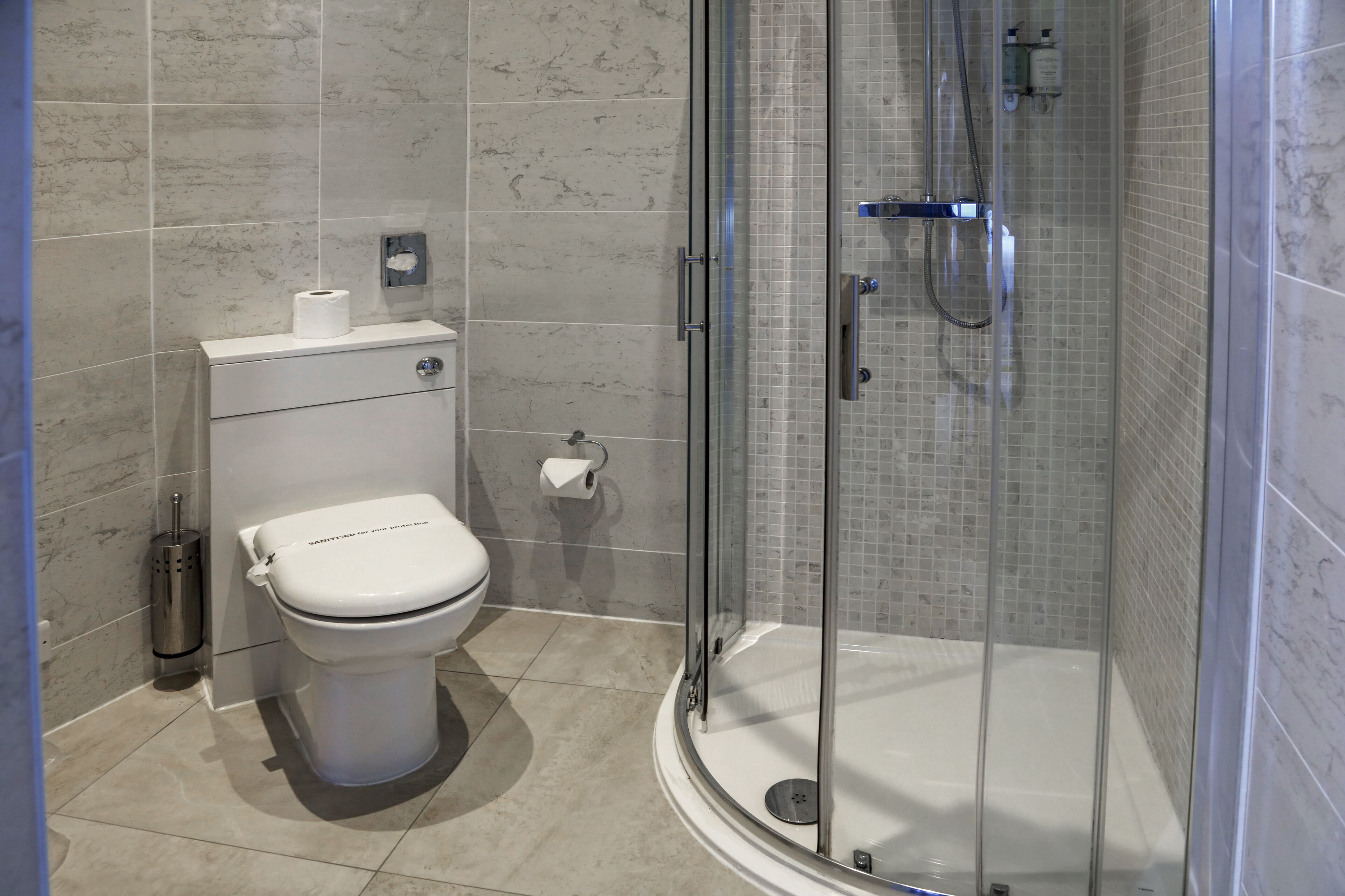 Une salle de bain moderne avec des toilettes, une douche à parois de verre et un mur recouvert de carreaux de marbre.
