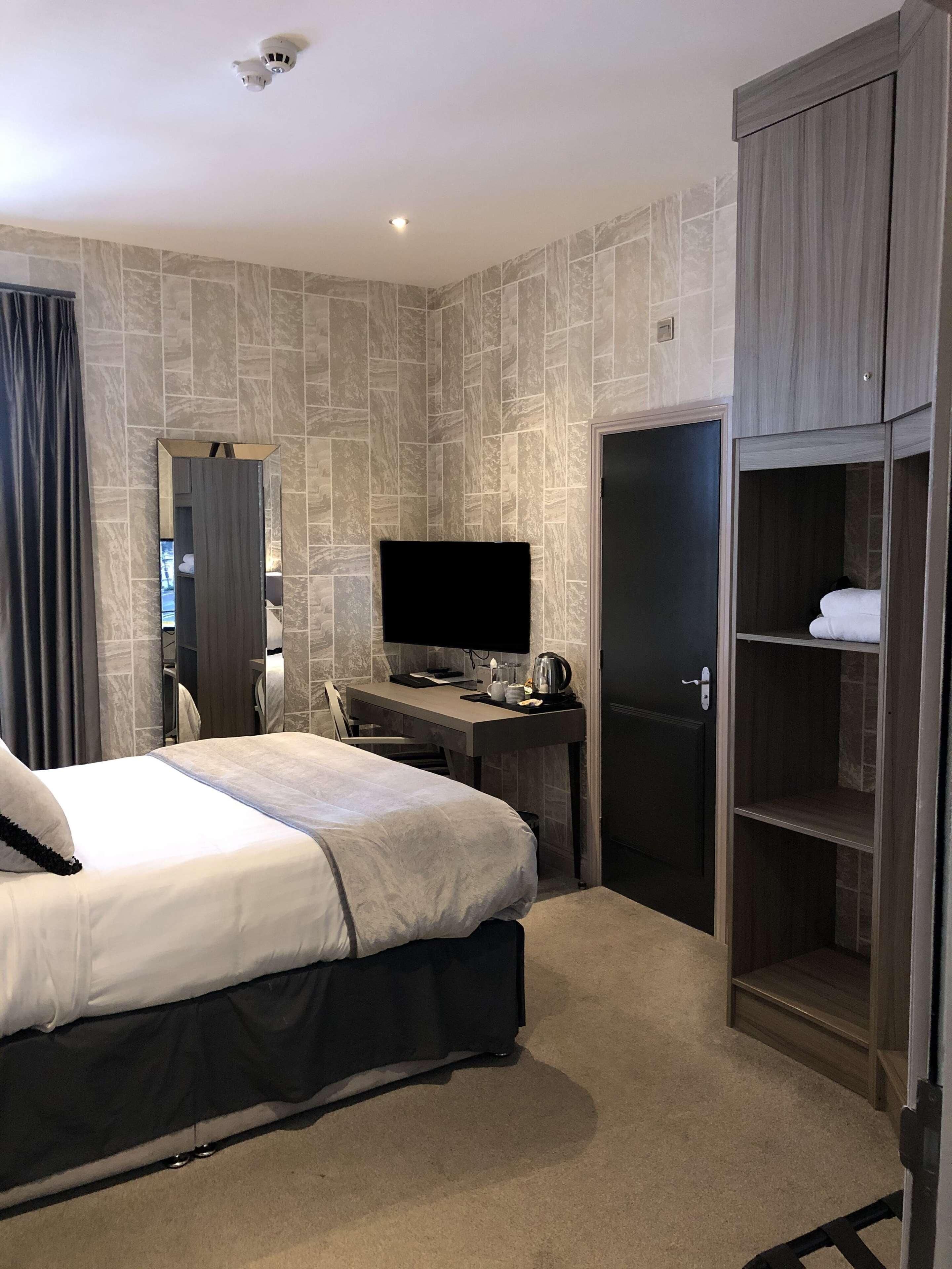 A hotel room with a bed, a desk with a computer, a wardrobe, and a mirror.