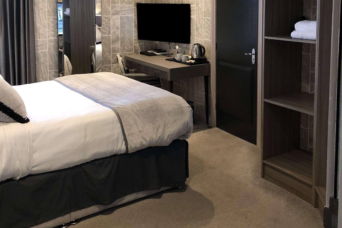 A hotel room with a bed, a desk with a computer, a wardrobe, and a mirror.