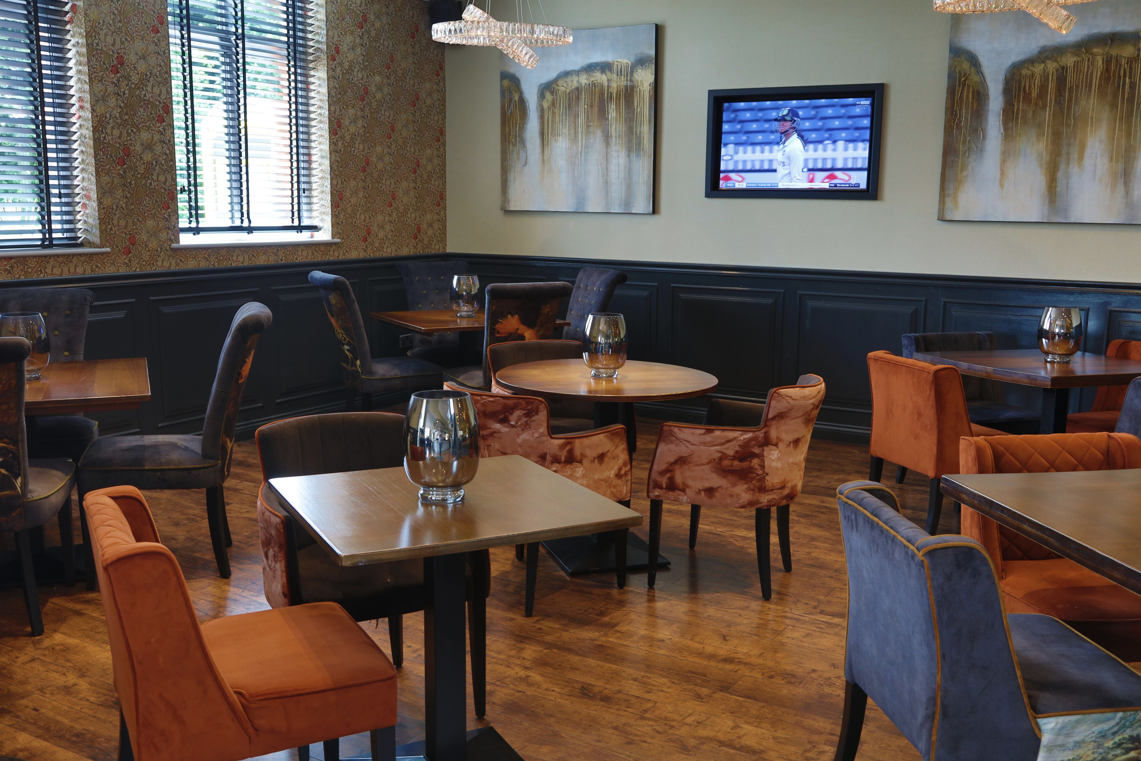 A restaurant interior with wooden tables and chairs, a television mounted on the wall, and artwork on the walls.