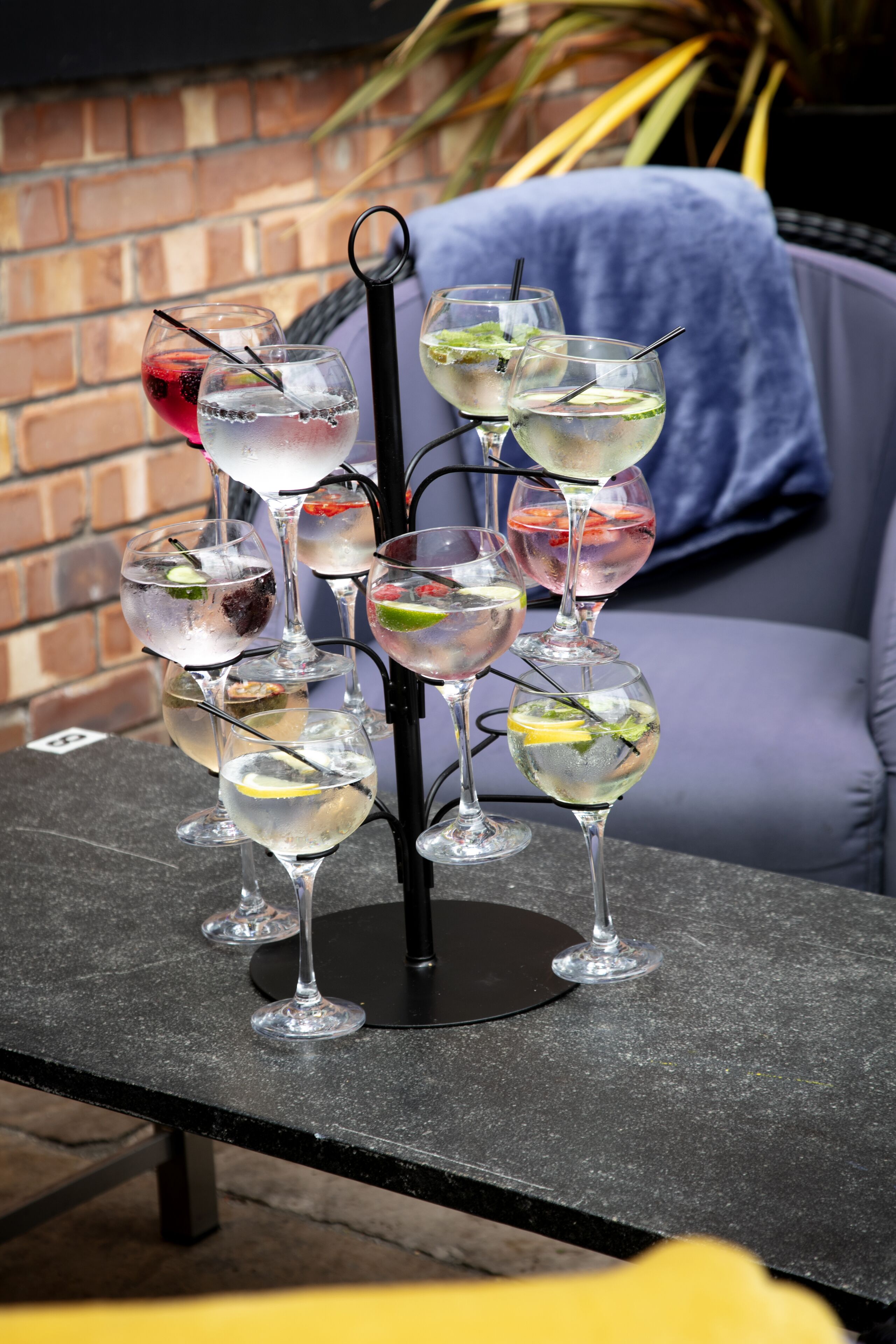 Ett bord med flera glas innehållande olika drycker, en tegelvägg och en blå soffa i bakgrunden.