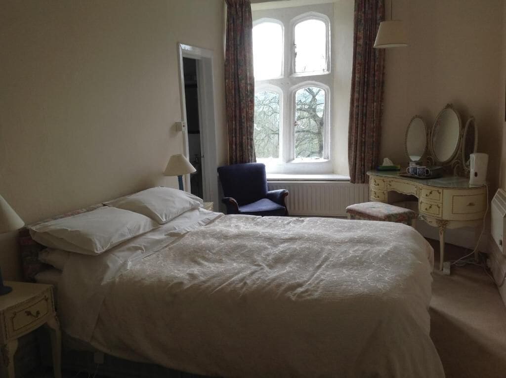 A bedroom with a bed, a chair, a dresser, a mirror, and a window with curtains.