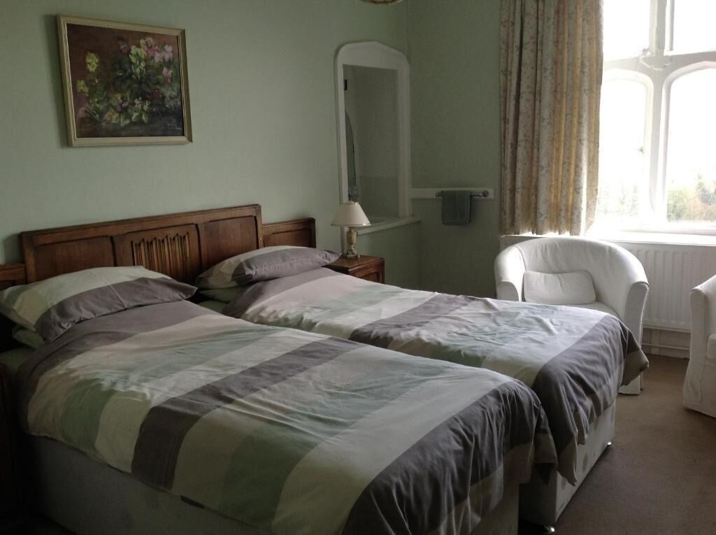 Een kamer met twee bedden, een stoel, een spiegel en een raam met gordijnen.