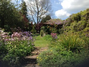 Un jardin avec un chemin de pierre, différentes plantes et une pergola recouverte de plantes grimpantes.