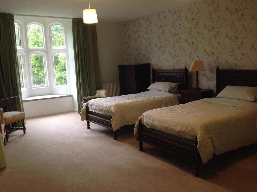 A room with two beds, a chair, a window with curtains, and a radiator.