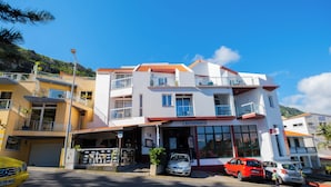 Un edificio de dos pisos con un restaurante en la planta baja. Varias automóviles están estacionados frente al edificio, y un auto amarillo es visible a la izquierda.