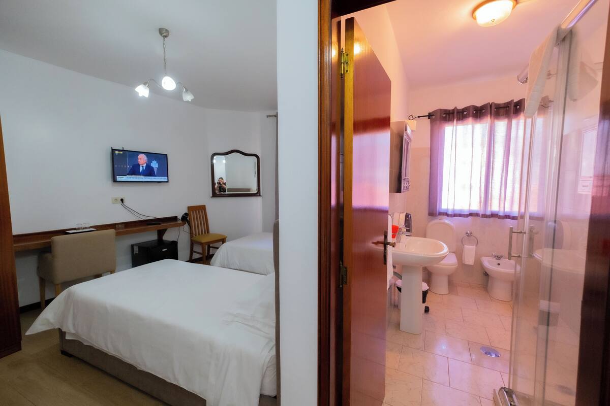 A hotel room with a bed, a desk, a television, a mirror, and a bathroom with a sink, toilet, and shower.