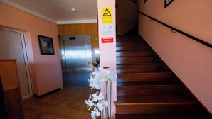Un pasillo de hotel con una escalera, un ascensor y una orquídea en maceta.