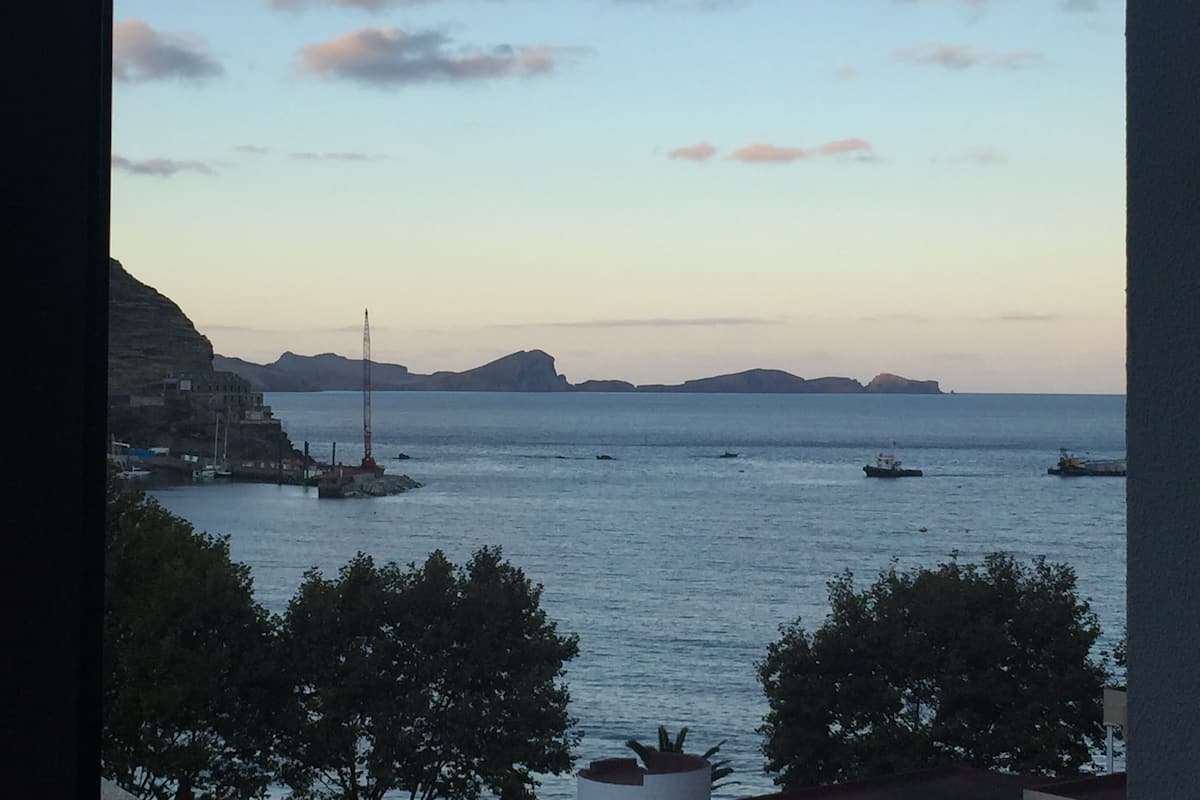 A coastal view with a lighthouse, boats, and distant landforms.