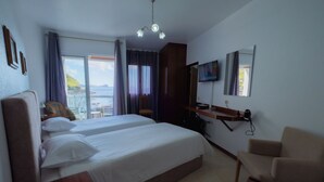 Habitación de hotel con dos camas, una silla, un televisor y vistas al mar.