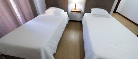 A hotel room with two single beds, a bedside table with a lamp, and a wooden floor.
