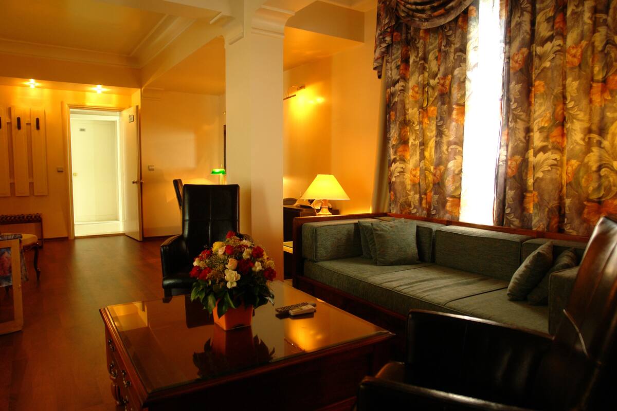 A living room with a sofa, a coffee table with a vase of flowers, a lamp, and a chair.