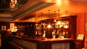 A bar area with a counter, stools, and a seating area with a glass table and chairs. - Kismet Hotel (Kusadasi)