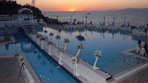 A poolside area with a sunset view, white chairs, and flower arrangements. - Kismet Hotel (Kusadasi)