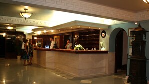 A lobby with a reception desk, a bar area, and a decorative clock. - Kismet Hotel (Kusadasi)