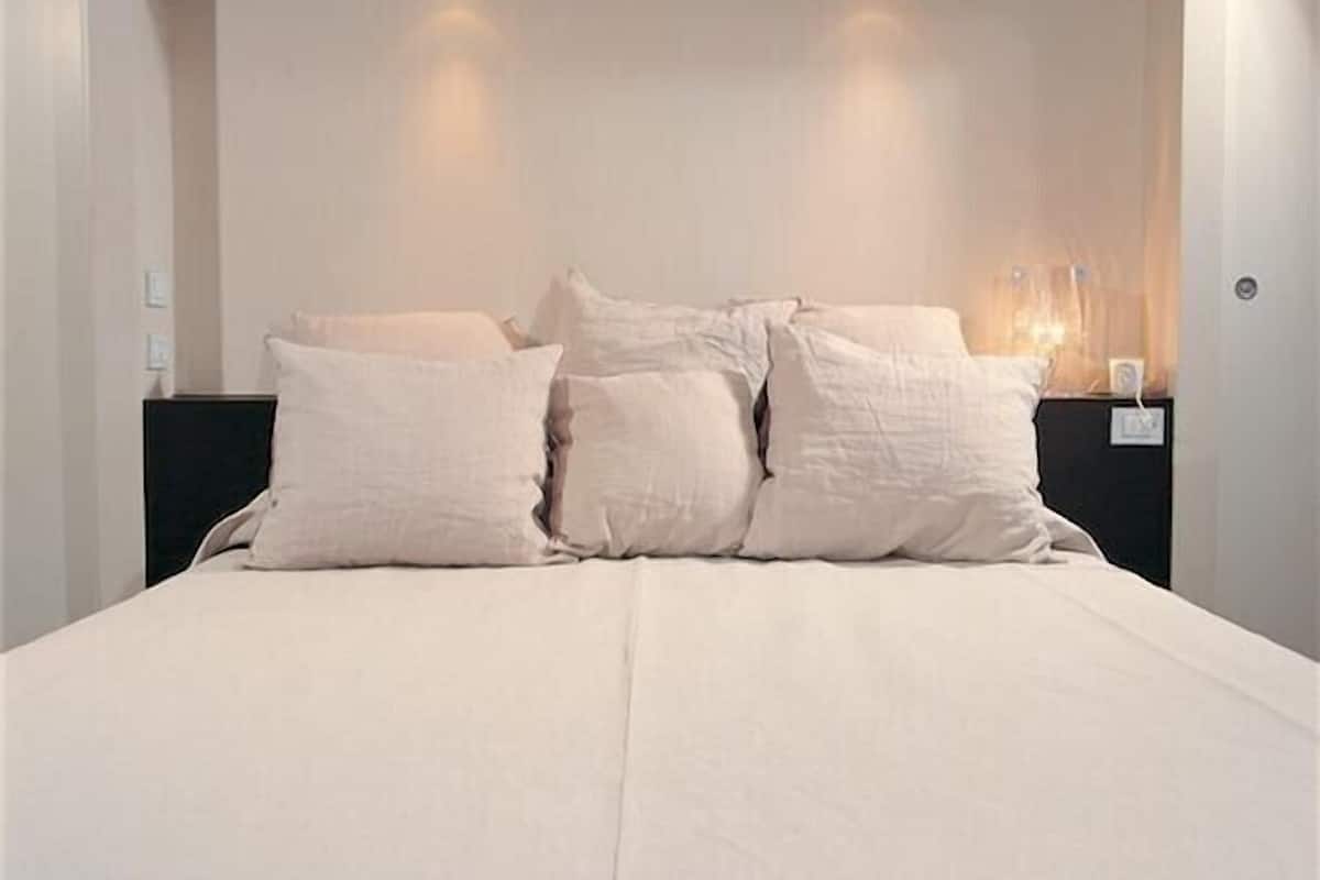 Een moderne slaapkamer met een groot bed, een hoofdbord met ingebouwde verlichting en een nachtkastje met een lamp.