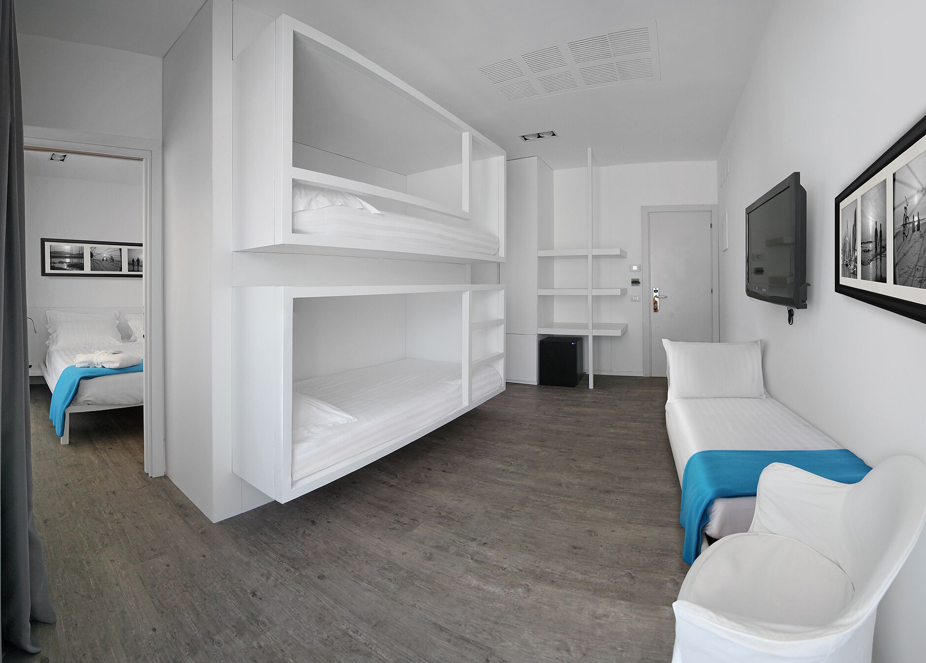Ein modernes, minimalistisches Schlafzimmer mit Etagenbett, Einzelbett, weißem Sofa und Wand-Fernseher.