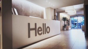 A reception desk with a 'Hello' sign, a potted plant, and a view of the outdoor area. - Hotel Europa Monetti (Cattolica)