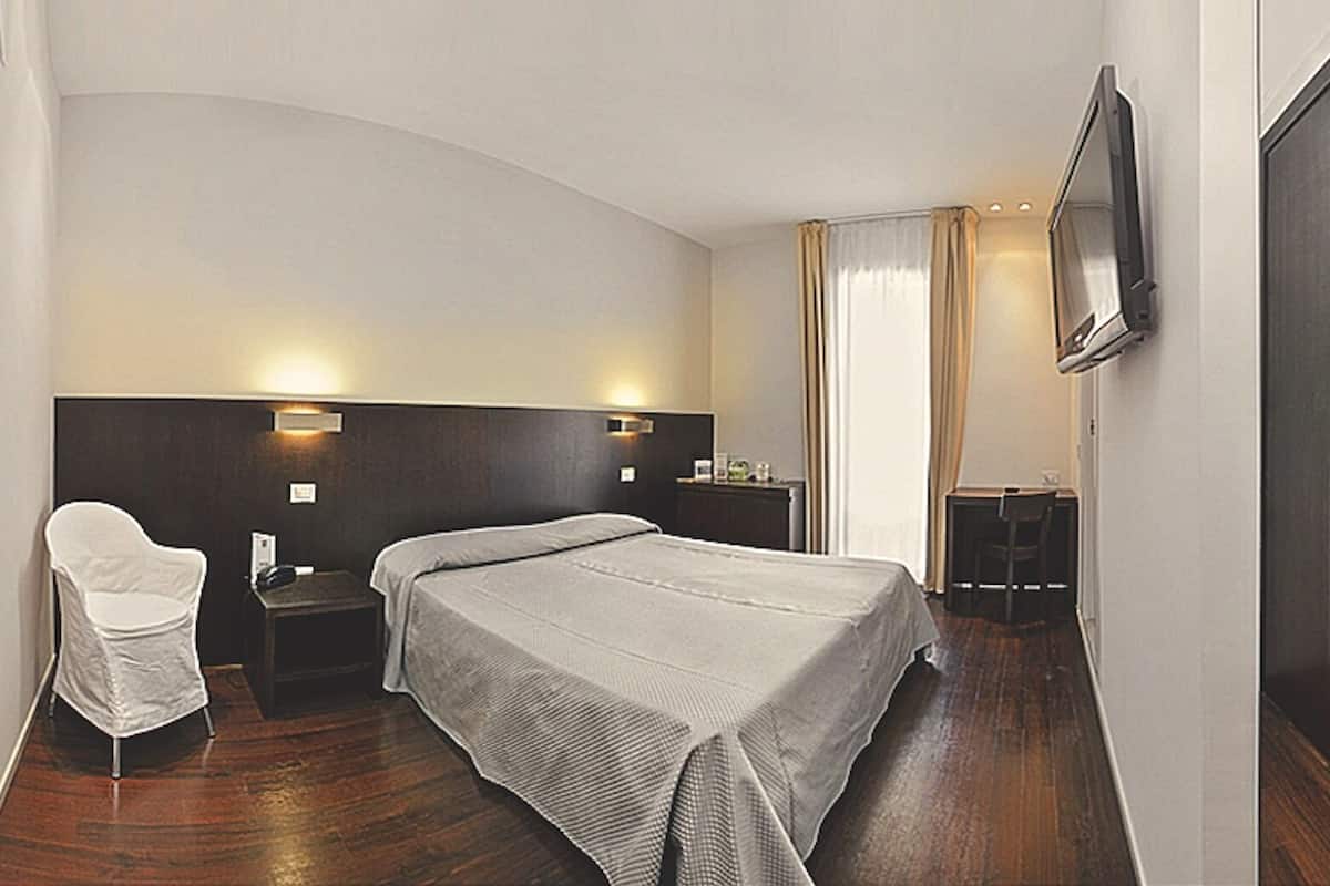 Een hotelkamer met een bed, een stoel, een bureau, een televisie en een raam met gordijnen.