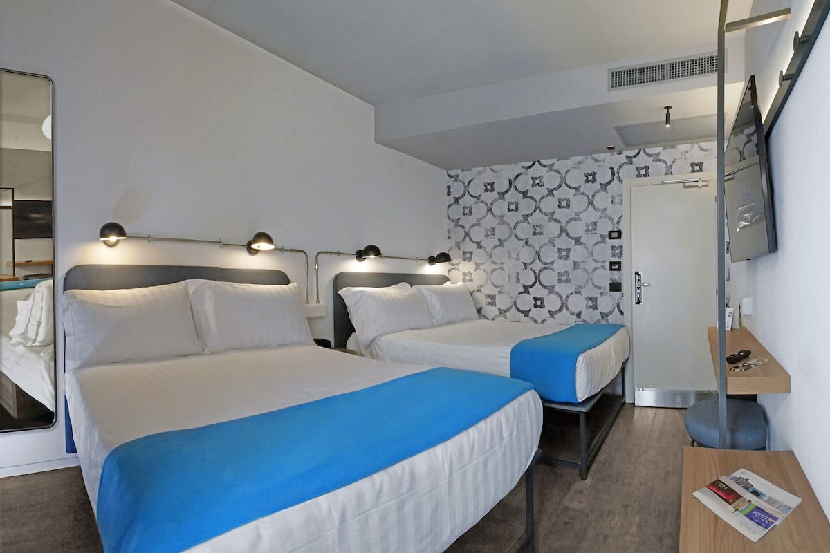 Een hotelkamer met twee bedden, een aan de muur bevestigde televisie, een klein tafeltje en een deur met een handdoekhouder.