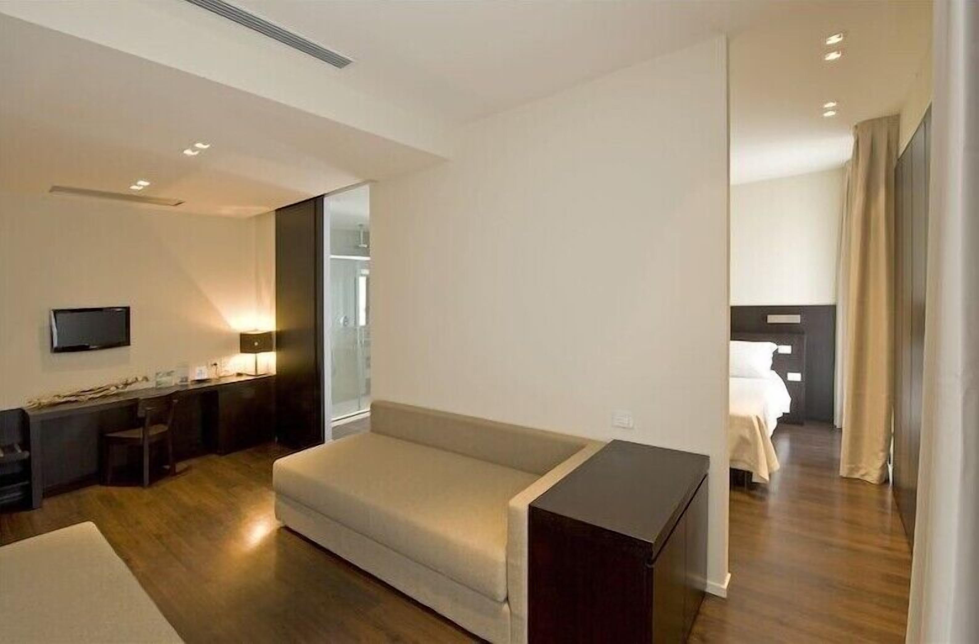 Una habitación de hotel moderna con sofá, escritorio con silla, televisor y cama.