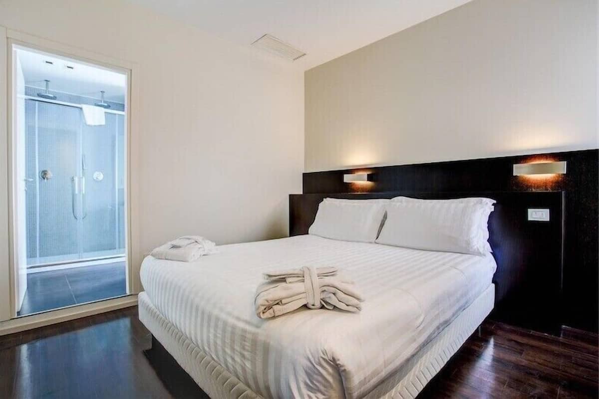 Hotelkamer met een bed, nachtkastje, wandlamp en een douchecabine van glas.