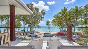 A balcony with a view of the beach, palm trees, and parked cars.