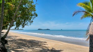 A beach with clear blue water, sandy shore, and palm trees.