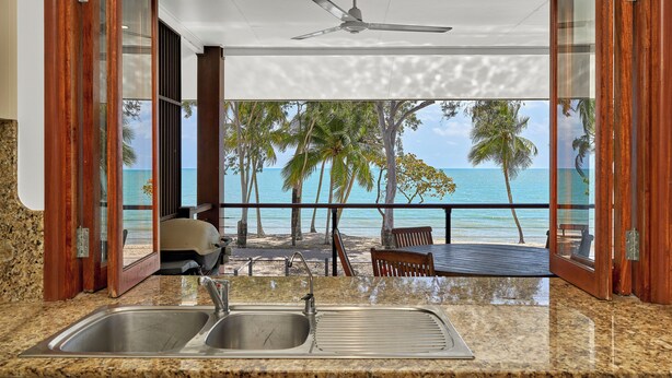 A kitchen with a view of the beach and palm trees.