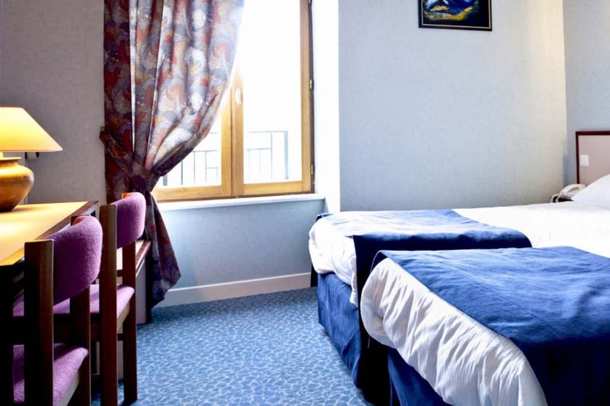 A hotel room with two beds, a desk with a lamp, and a window with curtains.