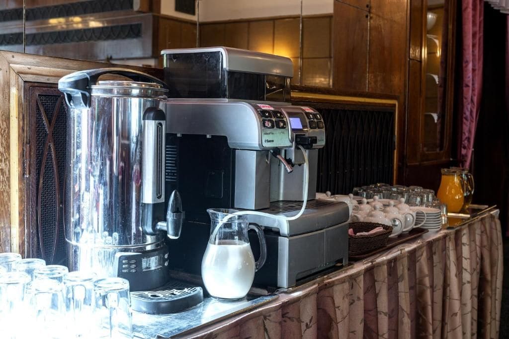 A coffee station with a coffee machine, milk pitcher, and various cups and mugs.